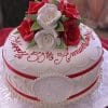 The AN-017 is a round white cake adorned with red and white roses, gold scalloped icing, and a red ribbon. "Happy 50th Anniversary" is written in red script on top, with the initials S E on the side.