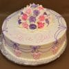 BB-011 is a round cake featuring pink and purple icing roses, white icing accents, "Its a Girl" written in pink frosting, and lavender and pink decorative icing along the sides.