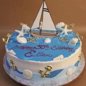 BD-070: Round nautical birthday cake features a sailboat topper, white seashells, gold anchors, blue icing, and "Happy 50th Birthday Ellen" written in red on top.
