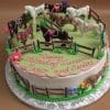 CB-012L: Round birthday cake with green icing, topped with small plastic horses, a brown fence, side flowers, and pink writing that says “Happy Birthday Zina, Mary, and Sonia.”.