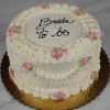 The BR-000H is a two-tiered white frosted cake with pink and green icing flowers, piped borders, and "Bride to be" written in black icing on top. It sits on a gold board.