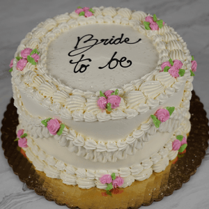 The BR-000H is a two-tiered white frosted cake with pink and green icing flowers, piped borders, and "Bride to be" written in black icing on top. It sits on a gold board.