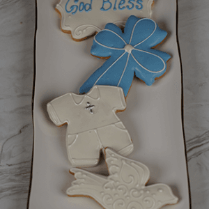 The CE-005c religious set features a rectangular plate of decorated cookies: a "God Bless" plaque, blue bow, white outfit with cross, and white bird on a marble surface.