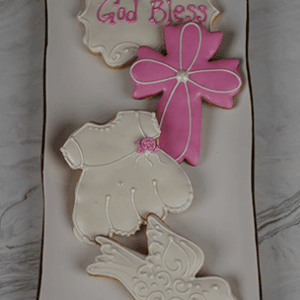The CE-005d religious set features four decorated cookies on a white tray: "God Bless" in pink icing, a pink cross, a white dress with a rose, and an ornate white dove.