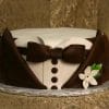 The GR-005 is a round cake styled as a tuxedo, featuring brown icing for the jacket, bow tie, and buttons, white icing for the shirt, and a small white flower with green leaves on the side.