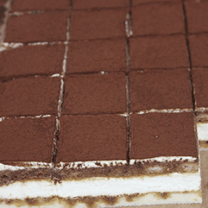 CO-002 Tiramisu 1X1 Bites: Tray of tiramisu cut into small, even squares, showing layers of creamy filling and cocoa powder on the sides.