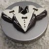 Three CE-003d bridal heart-shaped cookies, decorated with tuxedo-style white and black icing, are arranged on a silver cake stand against a textured white background.