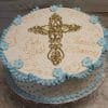 RC-020: Round white cake with a gold cross and "God Bless Charles Frances" in gold icing, decorated with blue ruffles and blue flower accents around the edge.