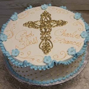 RC-020: Round white cake with a gold cross and "God Bless Charles Frances" in gold icing, decorated with blue ruffles and blue flower accents around the edge.
