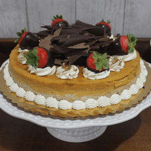 The GD-009 Pumpkin Cheesecake is topped with chocolate-dipped strawberries, whipped cream, and chocolate shavings, and displayed on a scalloped white cake stand.