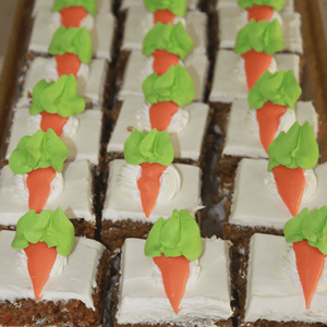 Rows of CO-075 Carrot Squares, each rectangular piece topped with white icing and decorated with orange and green carrot-shaped icing.