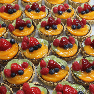 A tray of CO-023 3" Fruit Tarts, each topped with strawberries, raspberries, blueberries, kiwi slices, and a shiny glaze.