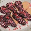 CE-020d Valentine's features heart-shaped cookies half-dipped in chocolate, topped with pink and white drizzle plus heart sprinkles, arranged on a white scalloped plate.