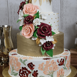 The WD-035 is a three-tiered cake featuring gold accents, a hand-painted floral bottom tier, quilted middle tier, and cascading fondant roses in pink, burgundy, and white with green leaves.