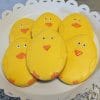Six oval-shaped CE-040c Easter cookies, decorated as yellow chicks with orange beaks and feet, are arranged on a white scalloped plate.