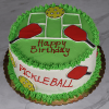 ST-000 is a round birthday cake featuring a green pickleball court, red paddles, yellow pickleballs, “Happy Birthday” on top, “PICKLEBALL” on the side, and finished with green icing trim.