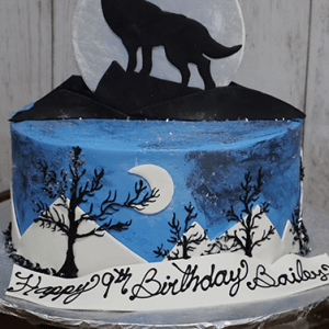 The CB-012P is a round cake featuring a howling wolf silhouette against a large moon, mountain shapes, and tree silhouettes. "Happy 17th Birthday Sailor" is written in black script icing.
