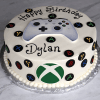 The CB-011N is a round birthday cake topped with an edible Xbox controller, colorful game controller buttons around the sides, and “Happy Birthday Dylan” written in black icing.