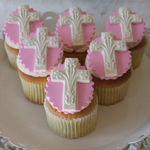 CC-039 Gold cupcakes with chocolate filling, topped with pink and white decorations featuring ornate white crosses, arranged on a white plate.