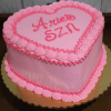 A BD-023A heart-shaped pink cake with piped frosting edges and "Aries SZN" in pink icing on top, presented on a gold cake board.