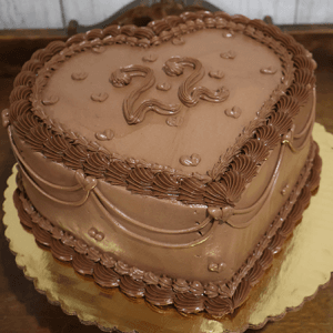 The CB-036B Heart Horoscope cake features a heart-shaped chocolate design with piped chocolate frosting, scalloped and swirled edges, small heart accents, and the number 22 on top, presented on a gold cake board.