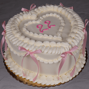 The BD-023F Heart shape one size cake is white, heart-shaped, decorated with pink bows, white piped frosting, and a pink "22" in the center, displayed on a gold cake board.