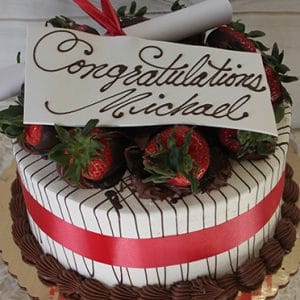 GC-002A is a decorated cake with white icing, chocolate stripes, chocolate-dipped strawberries, a red ribbon, and a “Congratulations Michael” card in cursive. A rolled-up parchment sits on top.