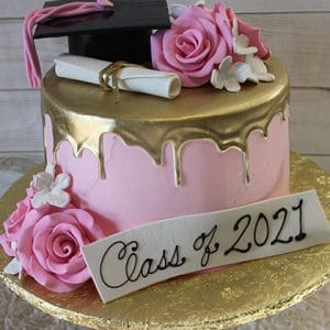 The GC-046 cake features pink and gold colors, topped with a graduation cap, diploma, pink roses, white flowers, and a plaque that says "Class of 2021" in black script.