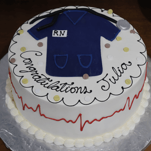 The GC-050B is a round cake topped with blue nurse scrubs, a stethoscope, and RN lettering. "Congratulations Julia" is written in black icing and a red heartbeat line circles the cake’s side.