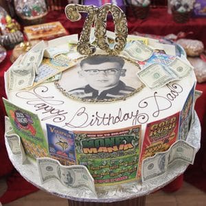The BD-092 cake is round and features a black-and-white photo of a man, gold "70" topper, faux dollar bills, colorful lottery ticket images, and "Happy Birthday Dad" inscribed in elegant script.