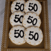 Six CE-001H Birthday cookies—round with white icing, gold trim, and a black "50"—are displayed on a rectangular gold tray with a decorative border.