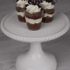 CO-100 Chocolate Shooters: Three small cups of layered chocolate and cream mousse, topped with whipped cream and chocolate pieces, arranged on a white beaded cake stand against a marble background.