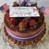 JC-006 Tiramisu topped with strawberries, chocolate shavings, mini American flags, and a "Happy July 4th" card. Red, white, and blue ribbon surrounds the cake for a festive patriotic look.