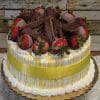 The BD-018F Mango cake is a round cake with white frosting, yellow drizzle, chocolate-dipped strawberries, chocolate shavings on top, and a yellow ribbon around the sides, displayed on a gold tray before a rustic wooden backdrop.