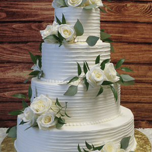 The WD-001A is a four-tiered white wedding cake with white roses, green leaves, textured horizontal icing lines, and a gold cake board, set against a wooden background.