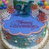 The SC-082 Luca cake features a round shape with blue icing, colorful balloons, coral accents, a dragon topper, and “Happy Birthday” in red icing. Floral and swirl decorations adorn the sides for a festive finish.