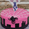 CB-005K is a pink cake with a white icing spiderweb, black fondant spider, black city silhouettes, and a Spider-Gwen superhero pose topper.
