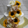 TC-007 is a two-tiered white cake with cascading sunflowers, white and blush roses, gold leaf accents on the sides, and set on a gold foil-covered base.