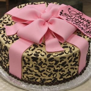 The BD-036B Cheetah Bow Pink is a round cake with a leopard print design, topped with a large pink fondant bow and a pink tag for your birthday message. Presented on a silver board.