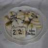 The CE-102a New Year set features decorated cookies shaped like party hats, clocks, and signs with 2024, CHEERS, and HAPPY NEW YEAR in black and gold icing on a white plate atop a marble surface.