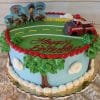 The SC-072 Paw Patrol cake is a round birthday cake decorated with a road, trees, clouds, PAW Patrol toppers, a toy fire truck, and "Happy Birthday" written in red icing on top.