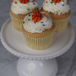 A CC-097B gold cupcake with chocolate filling is displayed on a white cake stand against a gray marble background.