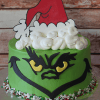 The CH-000E is a round cake shaped like the Grinch's face, featuring green frosting, yellow eyes, a fondant Santa hat with marshmallow-like topping, and red, green, and white sprinkles on a silver board.