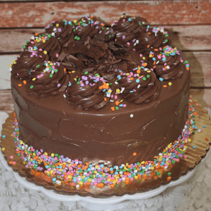 The BD-018J Gold cake with chocolate mousse filling features a round shape, swirled chocolate frosting, chocolate shavings, and confetti sprinkles on a gold cake board against a rustic wooden background.