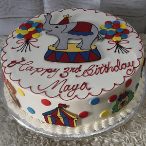 The CB-012M circus-themed birthday cake features an elephant topper, colorful balloons, a circus tent design, and “Happy 3rd Birthday Maya” written in red icing.