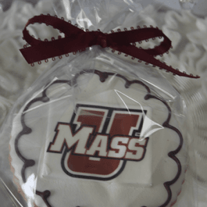 The GC-080E UMass Amherst is a round cookie with white icing, a maroon scalloped border, an edible UMass logo center, wrapped in clear plastic and tied with a maroon ribbon.