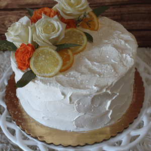 The BR-003 cake features white textured frosting, topped with white and orange roses plus lemon and orange slices, and is displayed on a white decorative stand with a gold base.