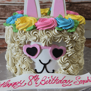 The CB-012D is a llama-themed birthday cake featuring colorful frosting flowers, pink heart-shaped sunglasses, upright ears, and "Happy 8th Birthday Sophia" written in pink icing.