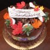 The THX-005 Display Tiramisu cake features chocolate shavings, autumn leaf decor, chocolate-dipped strawberries, and a white “Happy Thanksgiving” plaque in cursive, presented on a gold tray.