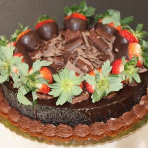 The GD-019 Chocolate Decadence Gluten Free is a chocolate cake adorned with chocolate shavings, chocolate-dipped strawberries, piped chocolate frosting around the base, and whole strawberries with green leaves along the edge.